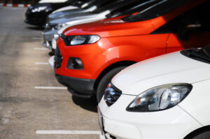 Closeup of front side of white car with other cars parking in parking lot in sunny day. The mean of simply transportation in modern world.